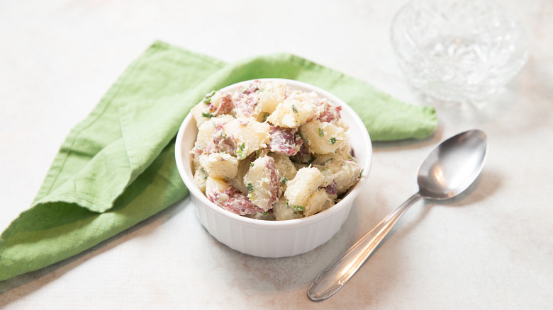 potato salad in small bowl next to napkin and spoon