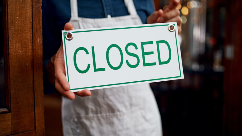 Person in apron holding a sign that says CLOSED in green letters on white background