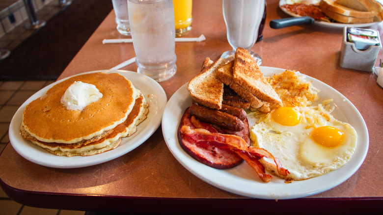 Classic diner breakfast spread of pancakes, fried eggs, bacon, hashbrowns, toast, and sausages