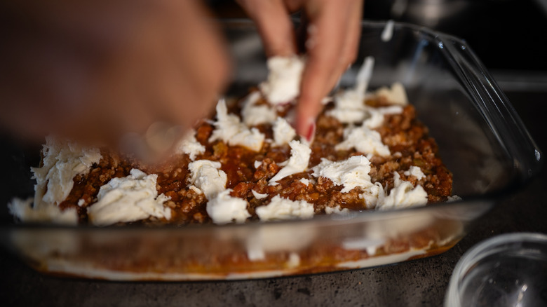 Person adding ricotta cheese to a lasagna dish