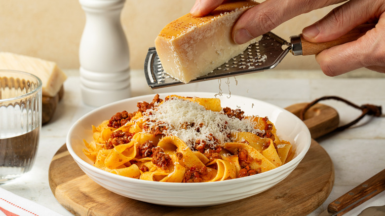 Person grating parmesan cheese over a bowl of spaghetti bolognese