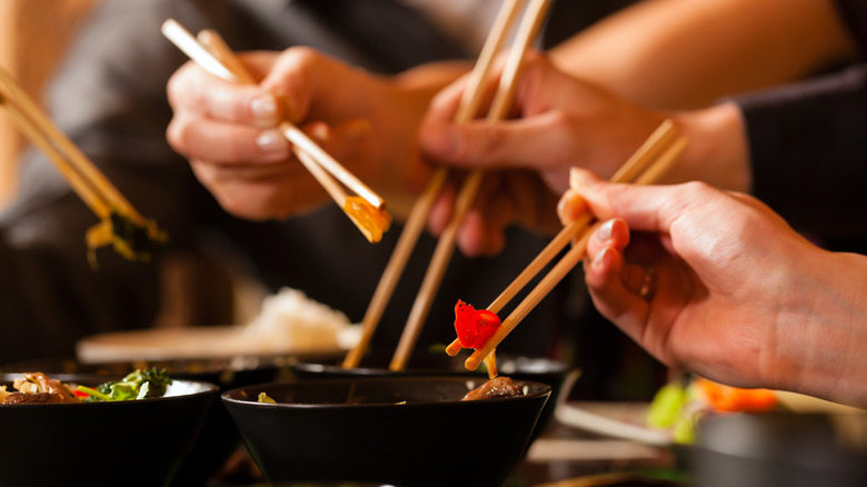 Various hands holding chopsticks in bowls of Chinese food