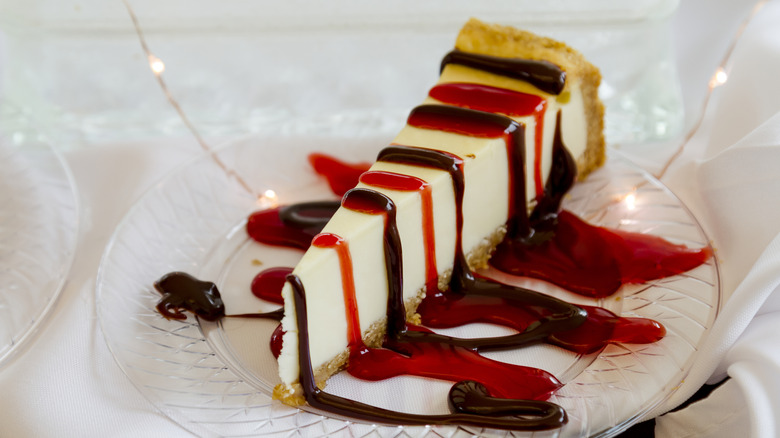 cheesecake topped with strawberry and chocolate drizzle on white plate