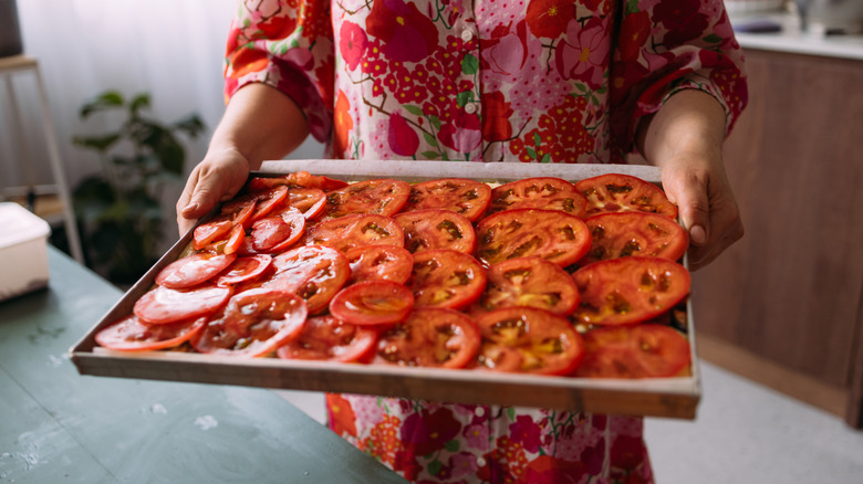 woman in floral dress holds out tray of sliced juicy tomatoes