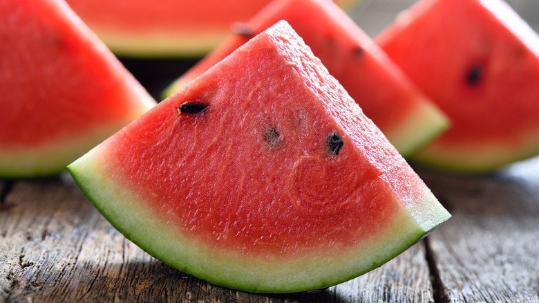 Close up on a sliced wedge of watermelon on a wooden table, with other slices out of focus in the background