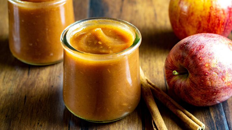 Jars of homemade apple sauce next to red apples and cinnamon sticks