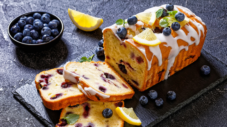 A lemon blueberry pound cake with glaze is set on a marble slab.