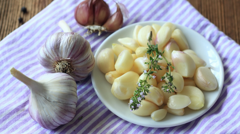 Thyme and garlic bulbs in plate on purple striped towel