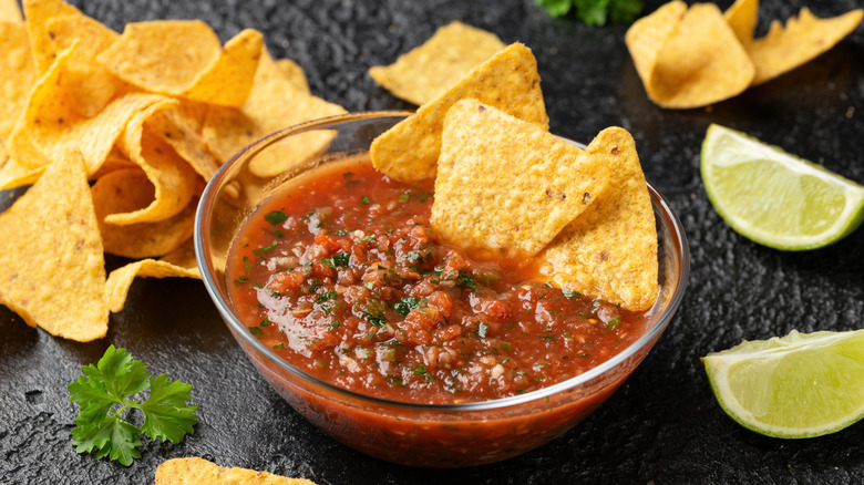 bowl of salsa with chips and lime wedges