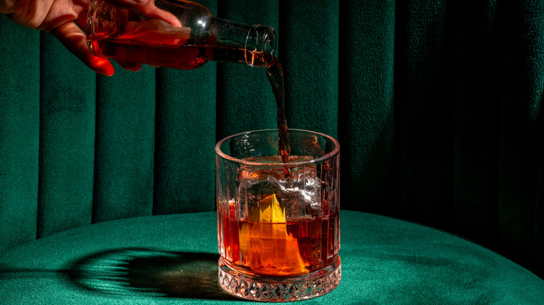 Closeup of person pouring spirit into a classic negroni cocktail