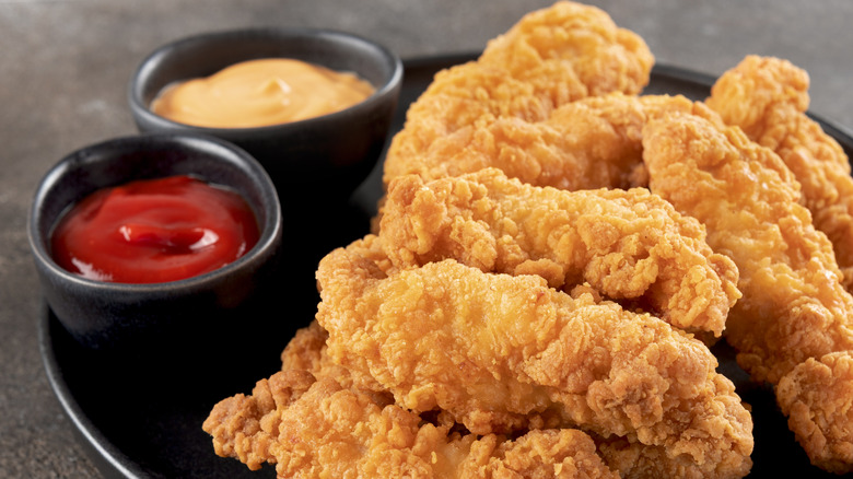 Crispy chicken breast strips with ketchup on a dark background