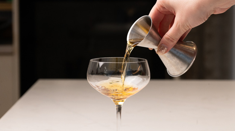 Hand using jigger to pour liquid into cocktail glass
