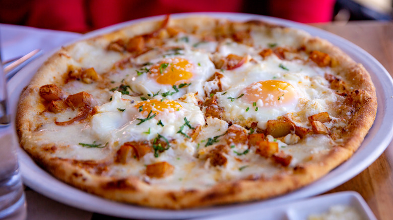 breakfast pizza topped with fried eggs on a plate on a wooden table