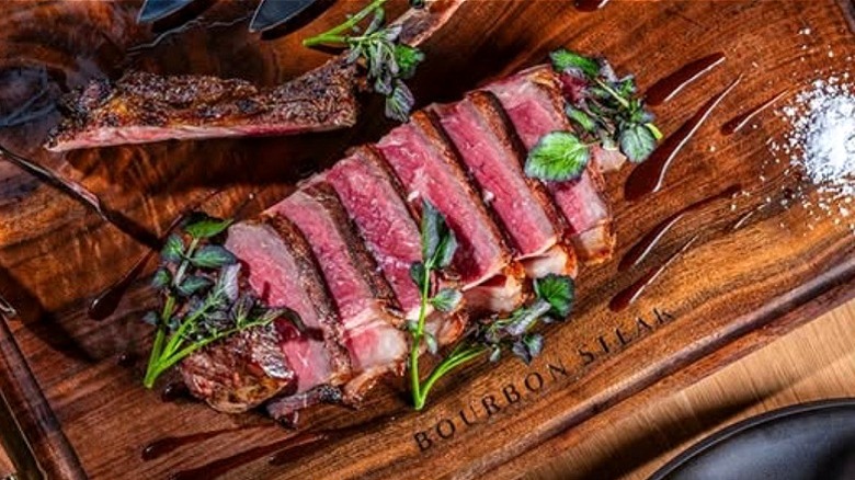 Slices of medium rare steak on Bourbon Steak cutting board.
