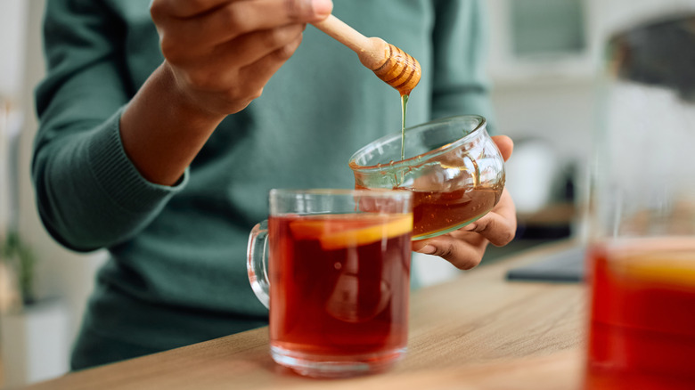 Someone adds a swirl of honey to a mug of tea