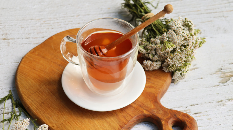warm honey in a small mug sits beside some fresh flowers