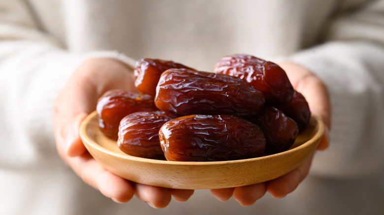 Hands holding wooden plate of dates