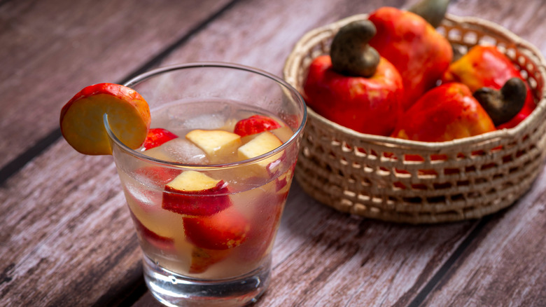 A cocktail containing cachaça and diced fruit sits on a wooden table next to a basket of fruit