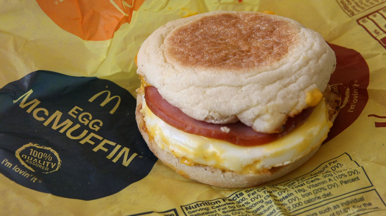 An Egg McMuffin with ham sitting on a yellow Egg McMuffin wrapper