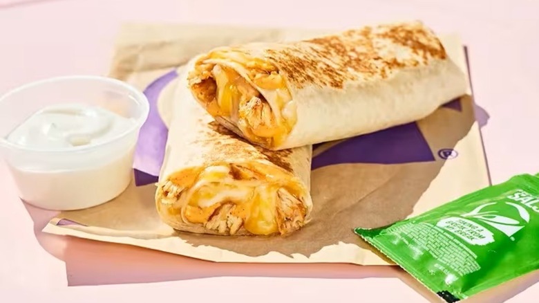 A Taco Bell rolled chicken quesadilla on a napkin next to a side of salsa verde and sour cream
