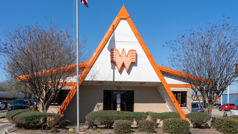 An A-frame Whataburger building with the logo on the outside, trees and shrubs surrounding