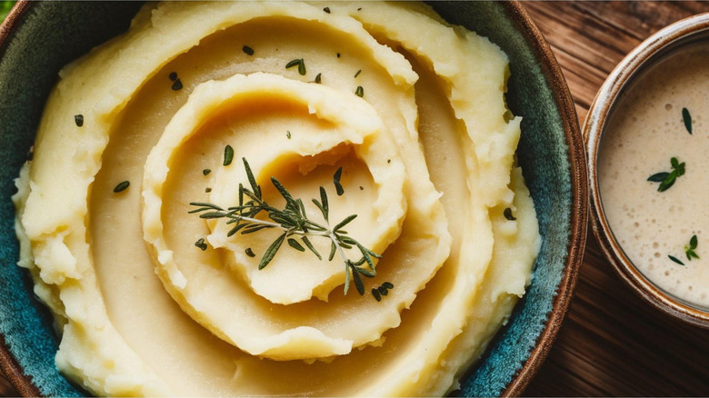 A bowl of creamy mashed potatoes topped with fresh rosemary