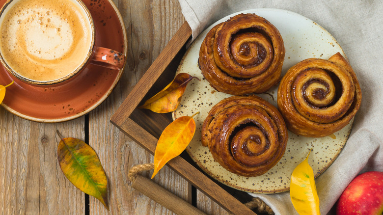 a tray of cinnamon rolls on a table with an autumn leaves and a cup of coffee