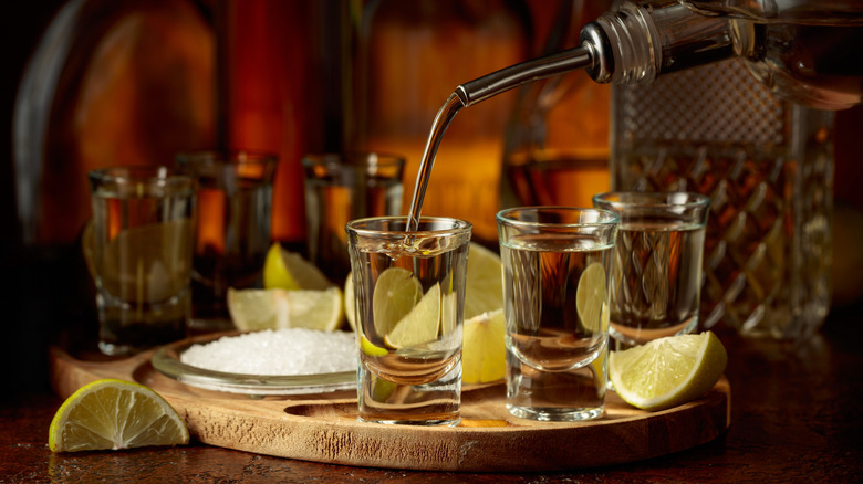 pouring light tequila into glasses surrounded by lime and salt