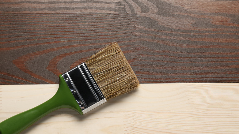 A brush resting on two wooden boards, one of which has been treated with a dark stain