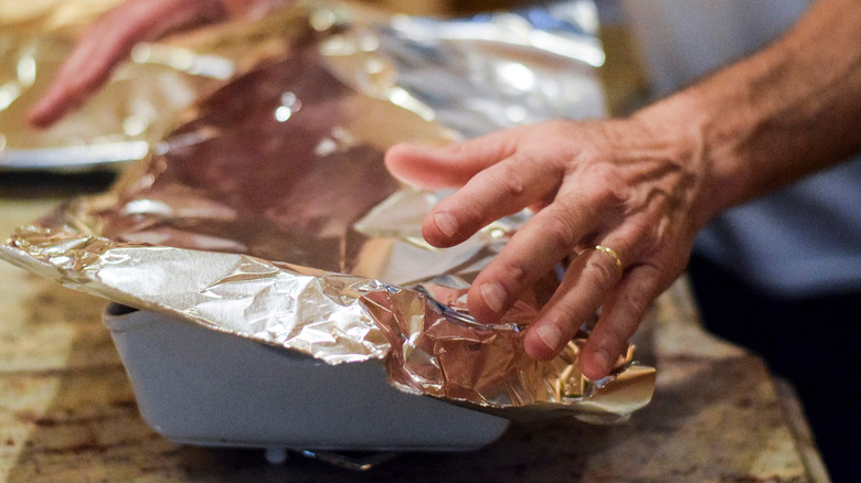 A person fits aluminum foil over a dish