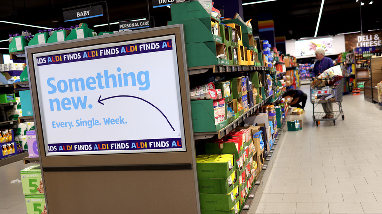 A shopper with a cart walking down an Aldi aisle and a sign that reads 
