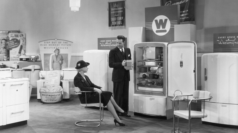 Black and white vintage photo of a salesman showing off a Westinghouse refrigerator to a seated woman
