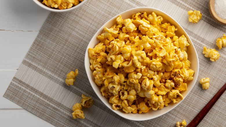 A white bowl of cheesy popcorn displayed on top of a brown and white placemat