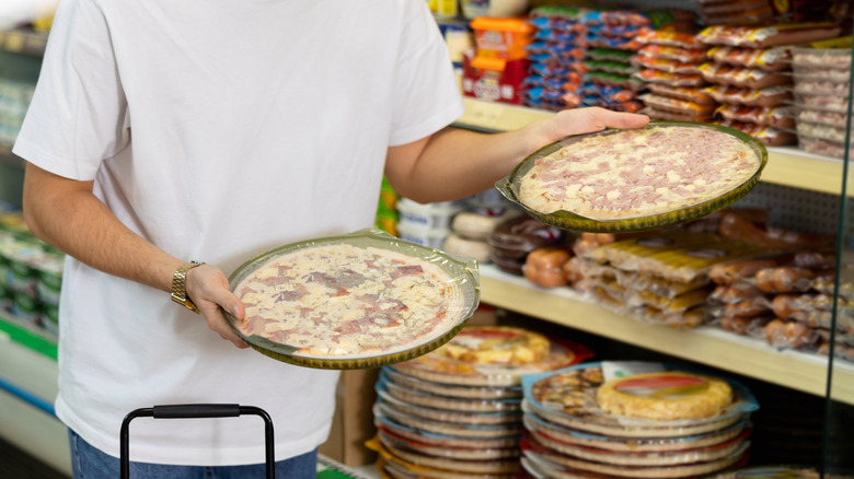 person in store aisle choosing between pizzas