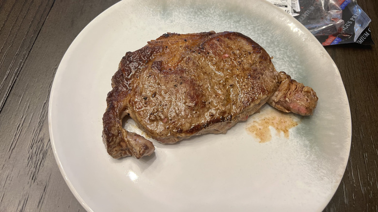 A cooked ribeye steak sits on a plate on a wooden table