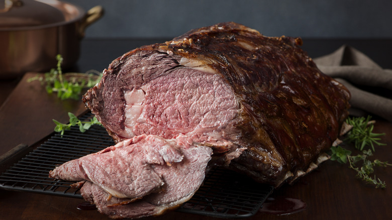 A partially sliced prime rib resting on a roasting rack on a kitchen table