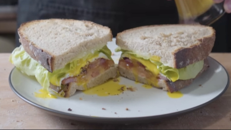 Two halves of an egg, bacon, cheese, tomato, and lettuce sandwich