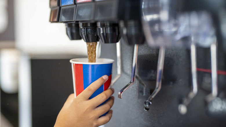 Person filling plastic cup with soda