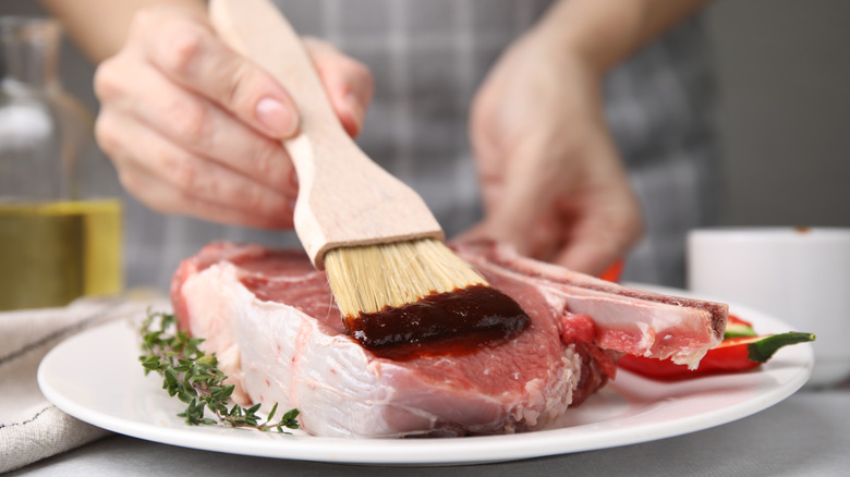 person adding marinade to steak with brush