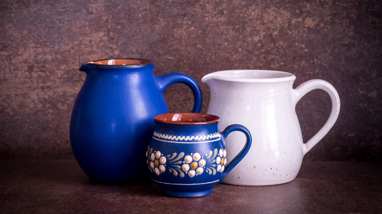 two ceramic pitchers and a clay mug on dark brown background