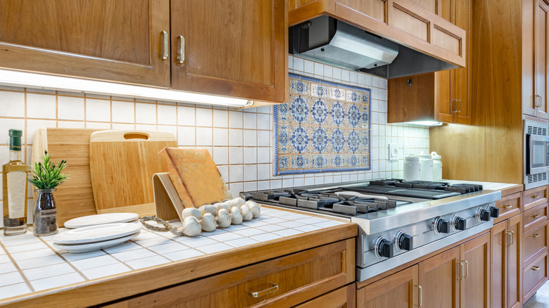 Kitchen with white tiled countertop and backsplash, with wooden cabinetry.