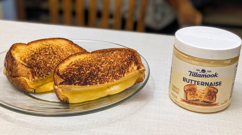 A grilled cheese sandwich on a glass plate and a jar of Butternaise on a white tablecloth