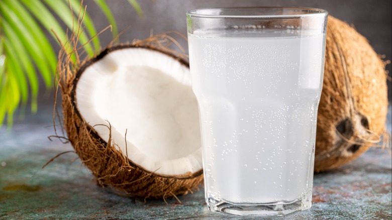 Coconut water in a glass with a fresh coconut in the background