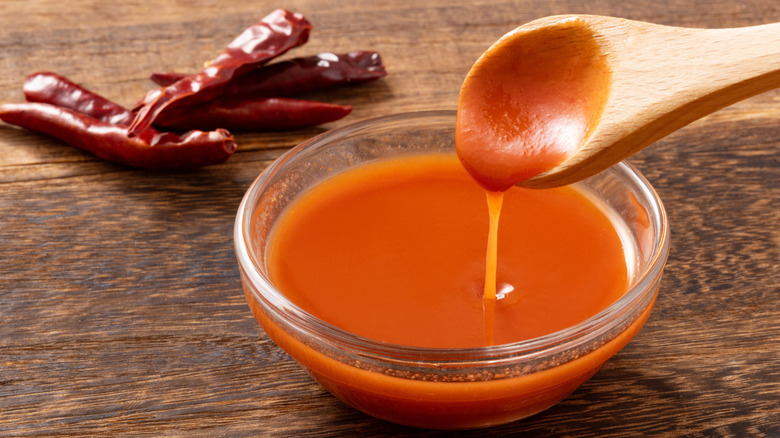 Tabasco sauce in a small glass bowl with a wooden spoon and chilies