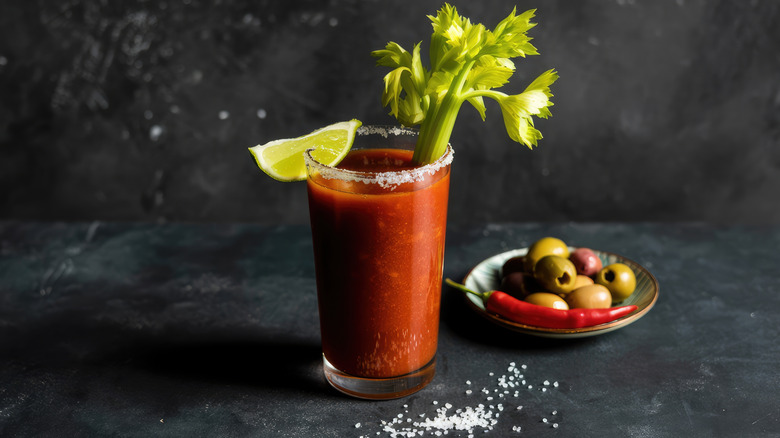Bloody mary with garnishes and a plate of olives on a black background