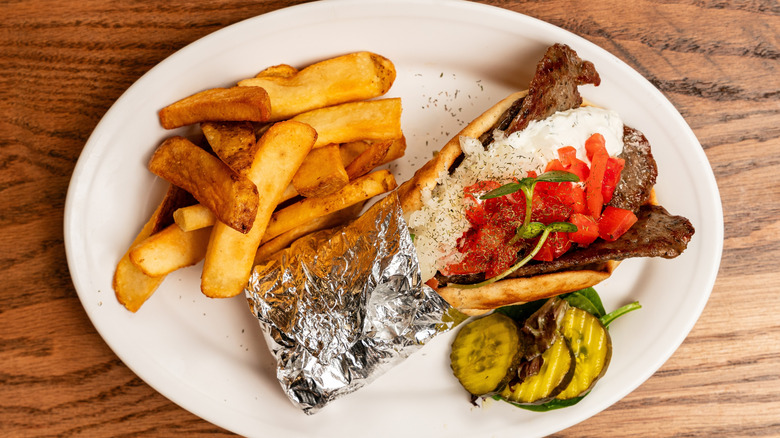 beef gyro in a pita with french fries and pickles on a plate