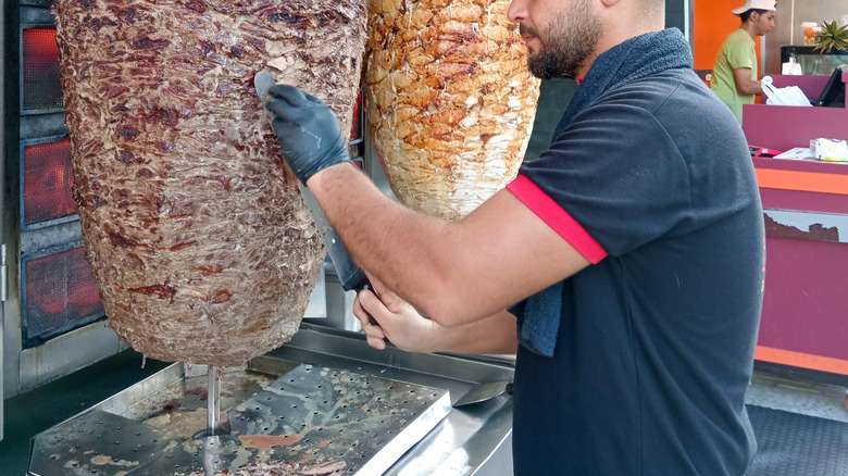 man carving meat from vetical spits