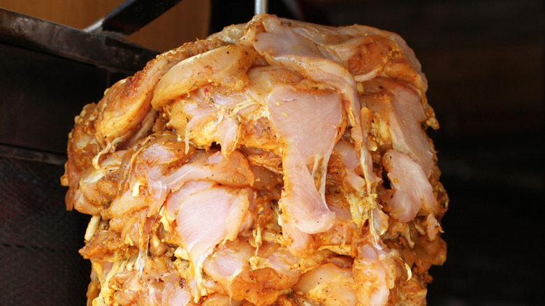 raw, marinated chicken slices stacked on a rotisserie spit