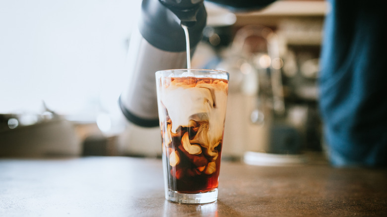 close up of a person pouring milk into a glass of iced coffee