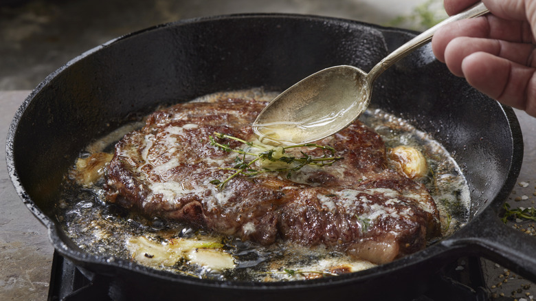 A steak sizzling in a pan with a spoon basting it with butter and pan juices